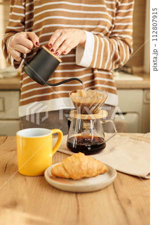 female makes coffee in morning kitchen. brews in purover. yellow cup with black coffee drip 112807915