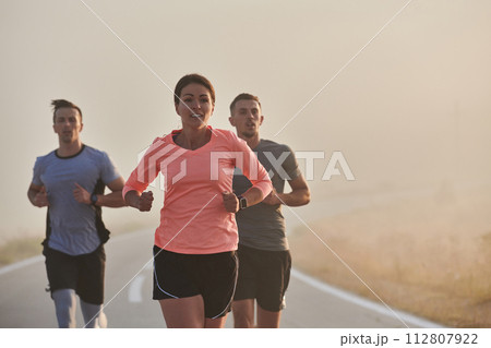 A group of friends, athletes, and joggers embrace the early morning hours as they run through the misty dawn, energized by the rising sun and surrounded by the tranquil beauty of nature 112807922