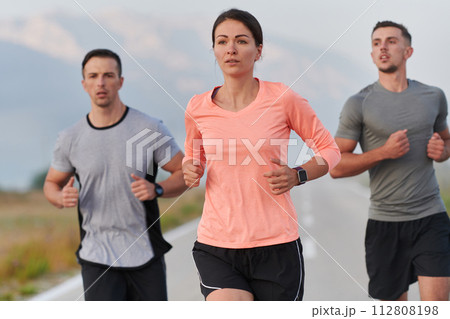 A group of friends, athletes, and joggers embrace the early morning hours as they run through the misty dawn, energized by the rising sun and surrounded by the tranquil beauty of nature A group of friends, athletes, and joggers embrace the early morning hours as they run through the misty dawn, energized by the rising sun and surrounded by the tranquil beauty of nature 112808198