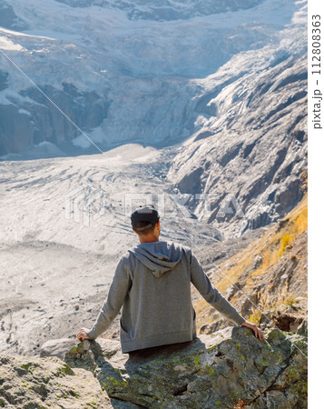 Man sitting on the rock in highest mountains. Mountain with glacier and tourist 112808363