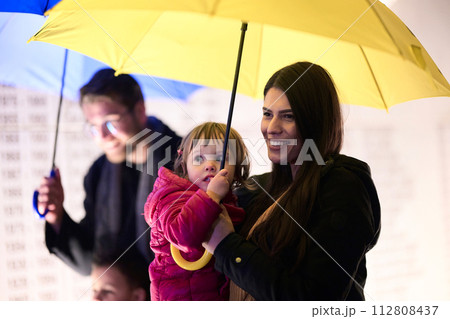 In the midst of a rainy urban night, a happy couple takes their children on a stroll through the city streets, heading towards the cinema for a delightful family movie outing 112808437