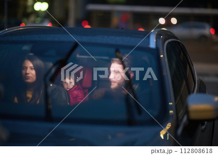 In the nighttime hours, a happy family enjoys playful moments together inside a car as they journey on a nocturnal road trip, illuminated by the glow of headlights and filled with laughter and joy 112808618