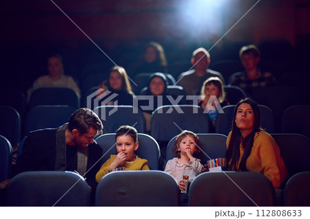 A modern family enjoys quality time together at the cinema, indulging in popcorn while watching a movie with their children 112808633