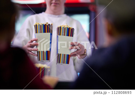 A vendor stands outside the cinema, holding freshly popped popcorn to sell to moviegoers before they enter the theater A vendor stands outside the cinema, holding freshly popped popcorn to sell to moviegoers before they enter the theater 112808693