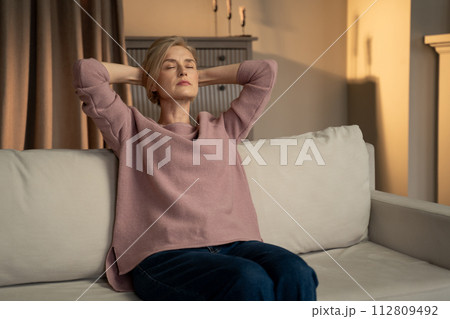 Woman Relaxing on a Sofa in a Cozy Living Room at Dusk Woman Relaxing on a Sofa in a Cozy Living Room at Dusk 112809492