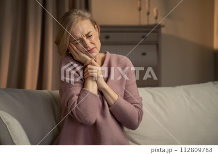 Mature Woman Sitting on Couch With Expression of Discomfort Due to Toothache 112809788