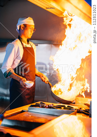 Chef hands with wok and fire. Closeup of chef cooking food with flames in professional kitchen. Expertise at work busy cooking handling flames in a modern setting. cook food with fire Chef hands with wok and fire. Closeup of chef cooking food with flames in professional kitchen. Expertise at work busy cooking handling flames in a modern setting. cook food with fire 112811023