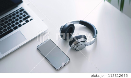 Modern tech gadgets, including sleek smartphone and stylish headphone, form a harmonious display on the spotless white surface Modern tech gadgets, including sleek smartphone and stylish headphone, form a harmonious display on the spotless white surface 112812656