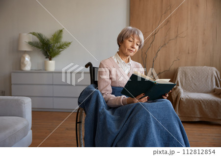 Retired woman with disability sitting in wheelchair reading book 112812854
