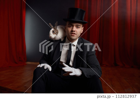 Showman in suit sitting on theatre stage resting after magic show 112812937