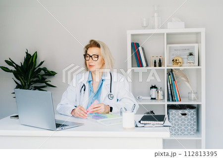 Friendly female middle aged doctor shows pills organizer to patient on laptop in clinic office. Video call online, treatment remote, pharmacy, supplement advice, medical healthcare. Telemedicine Friendly female middle aged doctor shows pills organizer to patient on laptop in clinic office. Video call online, treatment remote, pharmacy, supplement advice, medical healthcare. Telemedicine 112813395