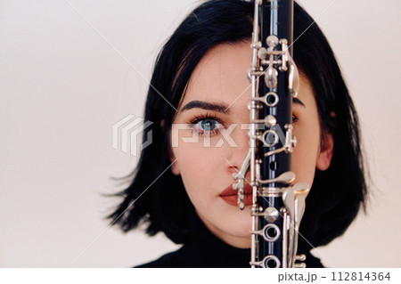 Graceful Brunette Musician Posing with Clarinet on White Background 112814364