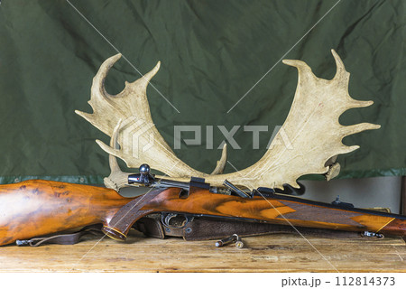 Beautiful hunting trophy deer antlers and hunting carbine on a wooden table Beautiful hunting trophy deer antlers and hunting carbine on a wooden table 112814373