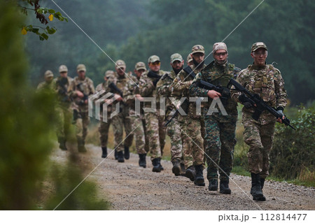 An elite military unit, led by a major, confidently parades through dense forest, showcasing precision, discipline, and readiness for high-risk operations An elite military unit, led by a major, confidently parades through dense forest, showcasing precision, discipline, and readiness for high-risk operations 112814477
