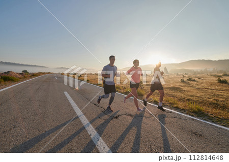 A group of friends, athletes, and joggers embrace the early morning hours as they run through the misty dawn, energized by the rising sun and surrounded by the tranquil beauty of nature 112814648