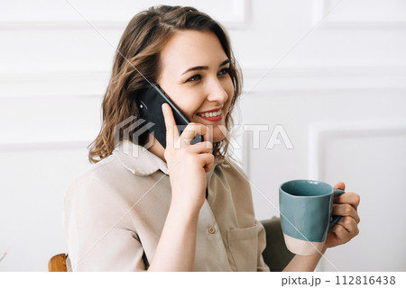 Happy Young Woman Enjoying a Phone Call While Savoring a Drink in Leisure Time. Joyful Young Woman 112816438