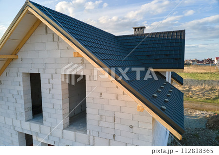 Aerial view of unfinished house with aerated lightweight concrete walls and wooden roof frame covered with metallic tiles under construction. Aerial view of unfinished house with aerated lightweight concrete walls and wooden roof frame covered with metallic tiles under construction. 112818365