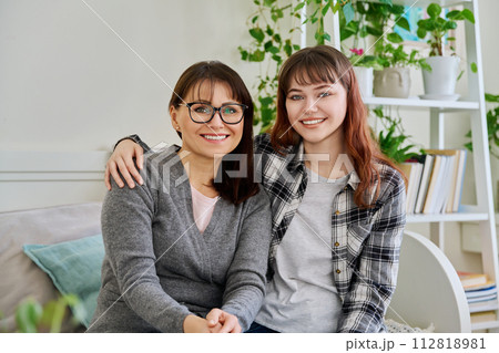 Portrait of happy hugging mother and teenage daughter sitting together on couch 112818981