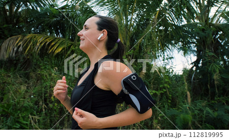 Young woman with headphones running along tropical trees, healthy lifestyle concept Young woman with headphones running along tropical trees, healthy lifestyle concept 112819995