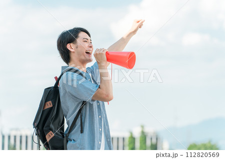 青空の下でメガホンで応援・声援・エールを送る若いアジア人男性・大学生・高校生・学生 112820569