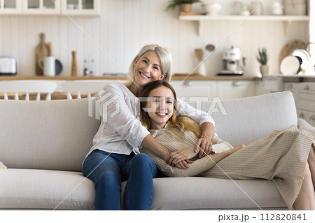 Mature mother cuddling preteen daughter resting in living room 112820841