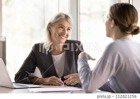 Millennial and middle-aged businesswomen having conversation in company office Millennial and middle-aged businesswomen having conversation in company office 112821256