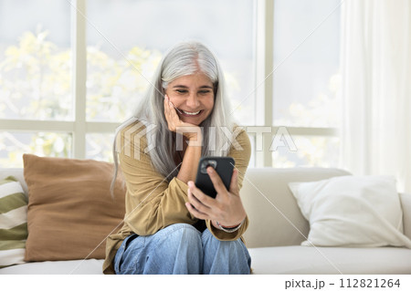 Happy elderly Hispanic woman watching online content on mobile phone 112821264