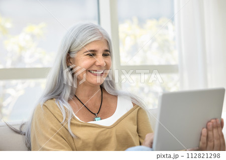 Happy elder woman using tablet for online communication at home 112821298