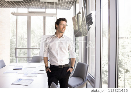 Businessman standing alone in modern conference room staring out window Businessman standing alone in modern conference room staring out window 112821436