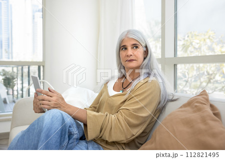 Serious pensive grey haired senior woman holding digital tablet Serious pensive grey haired senior woman holding digital tablet 112821495