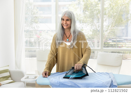 Happy cheerful older Hispanic housemaid woman doing housework 112821502