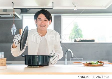 キッチンで鍋の蓋を開ける若い男性(料理教室・手料理・料理男子) キッチンで鍋の蓋を開ける若い男性(料理教室・手料理・料理男子) 112821898