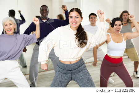 Smiling young woman rehearsing modern dance with group in dance school 112822880