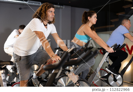Man and woman taking indoor cycling class at fitness center, doing cardio riding bike 112822966