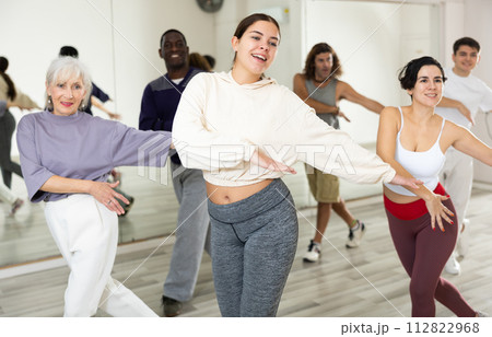 Smiling young woman rehearsing modern dance with group in dance school 112822968