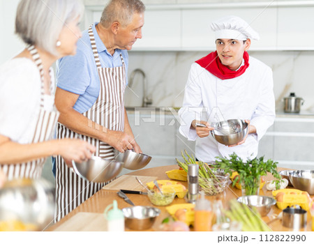 Positive young man chef of cooking course teaching attendees how to mix sauce Positive young man chef of cooking course teaching attendees how to mix sauce 112822990