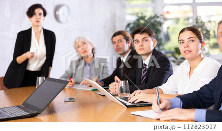 Focused colleagues of different ages discussing ideas and watching presentation while Latin female turning on presentation in meeting room Focused colleagues of different ages discussing ideas and watching presentation while Latin female turning on presentation in meeting room 112823017