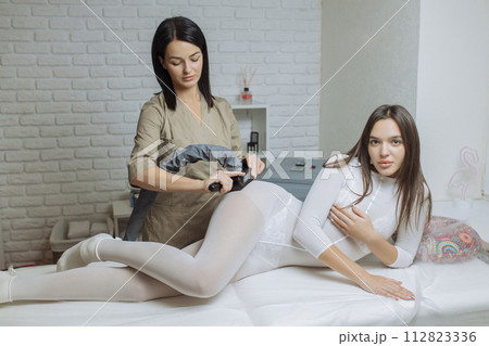 Woman in special white suit getting anti cellulite massage in a spa salon. LPG, and body contouring treatment in clinic.Reset body weight with LPG massage 112823336