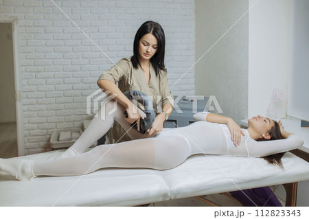 Woman in special white suit getting anti cellulite massage in a spa salon. LPG, and body contouring treatment in clinic.Reset body weight with LPG massage Woman in special white suit getting anti cellulite massage in a spa salon. LPG, and body contouring treatment in clinic.Reset body weight with LPG massage 112823343