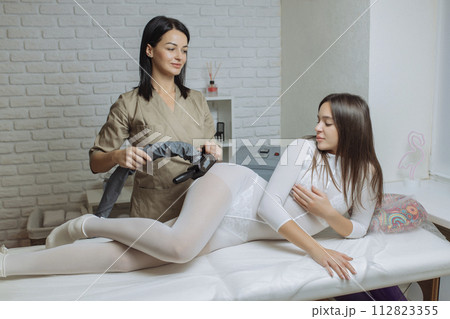 Woman in special white suit getting anti cellulite massage in a spa salon. LPG, and body contouring treatment in clinic.Reset body weight with LPG massage Woman in special white suit getting anti cellulite massage in a spa salon. LPG, and body contouring treatment in clinic.Reset body weight with LPG massage 112823355