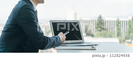 パソコンを使い説明・提案するスーツ姿のアジア人男性（詐欺師・不動産投資詐欺・ワンルーム詐欺） 112824938