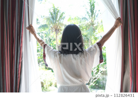 Morning of a new day, alarm clock wake up woman sitting in the room. A woman stretch the muscles at window. Health and care concepts Morning of a new day, alarm clock wake up woman sitting in the room. A woman stretch the muscles at window. Health and care concepts 112826431