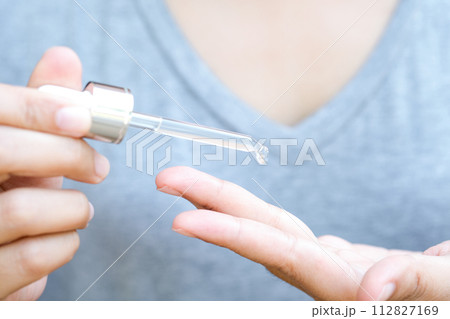 hands of a beautiful woman Dropping serum collagen moisturizer of face into clear gold bottle soft light background. Protector skin Treatment facial essence oil, Vitamin C. Beauty and spa Concept 112827169