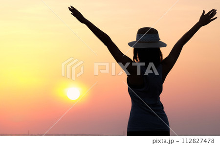The silhouette of a dreamy girl looking up at the horizon. woman watching the sunset by the sea Raise your hand to welcome the fresh air in the evening. The silhouette of a dreamy girl looking up at the horizon. woman watching the sunset by the sea Raise your hand to welcome the fresh air in the evening. 112827478
