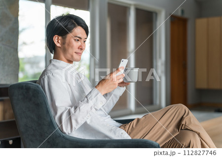 家でコーヒーを飲みながらスマホを見る若いアジア人男性 家でコーヒーを飲みながらスマホを見る若いアジア人男性 112827746