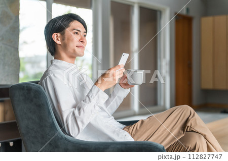 家でコーヒーを飲みながらスマホを見る若いアジア人男性 家でコーヒーを飲みながらスマホを見る若いアジア人男性 112827747
