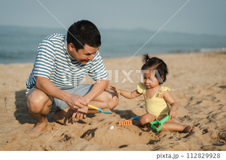 happy toddler baby girl playing sand toy with father on the sea beach 112829928
