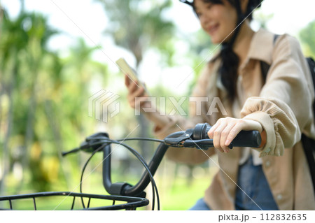 Cropped shot of smiling young woman using mobile phone while sitting on a bicycle Cropped shot of smiling young woman using mobile phone while sitting on a bicycle 112832635