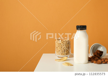 Bottle of alternative milk, nuts and soybeans on orange background, space for text Bottle of alternative milk, nuts and soybeans on orange background, space for text 112835573