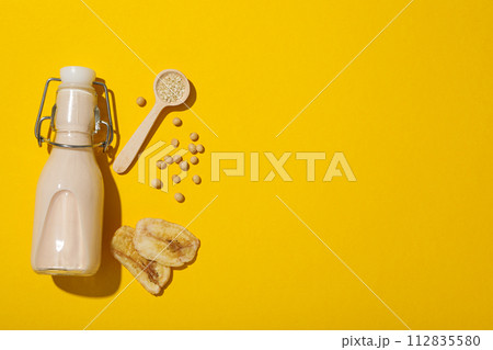 Bottle of alternative milk, soybeans and sliced bananas on yellow background, space for text Bottle of alternative milk, soybeans and sliced bananas on yellow background, space for text 112835580